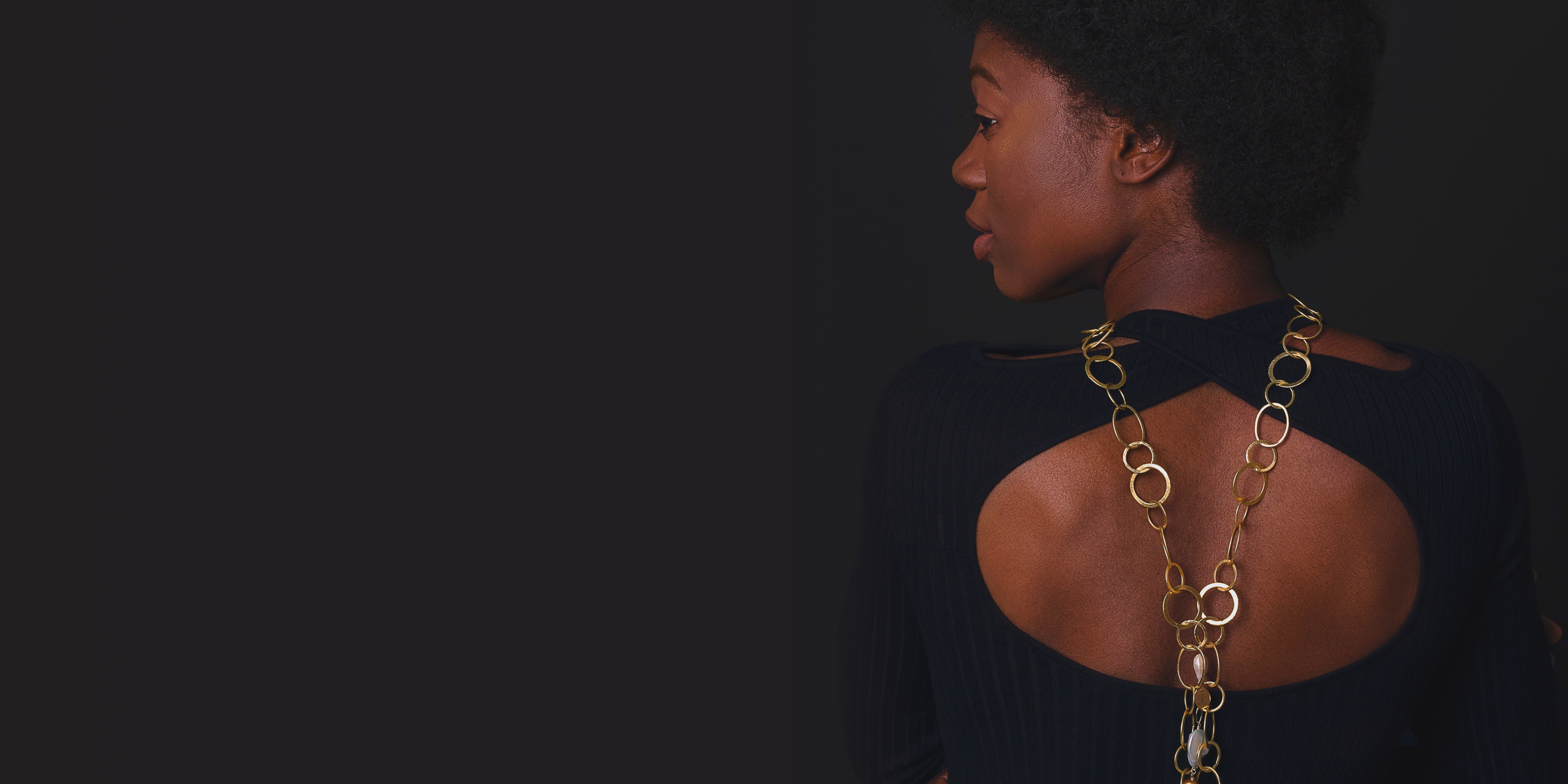 A woman wearing a long necklace showing her back